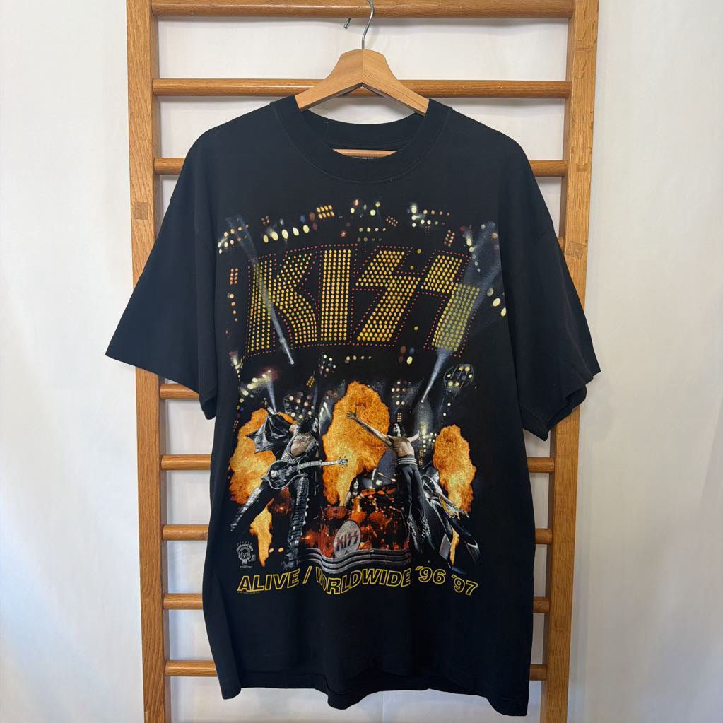 A black KISS 'Alive' graphic t-shirt hanging on a wooden hanger against a wooden ladder rack.