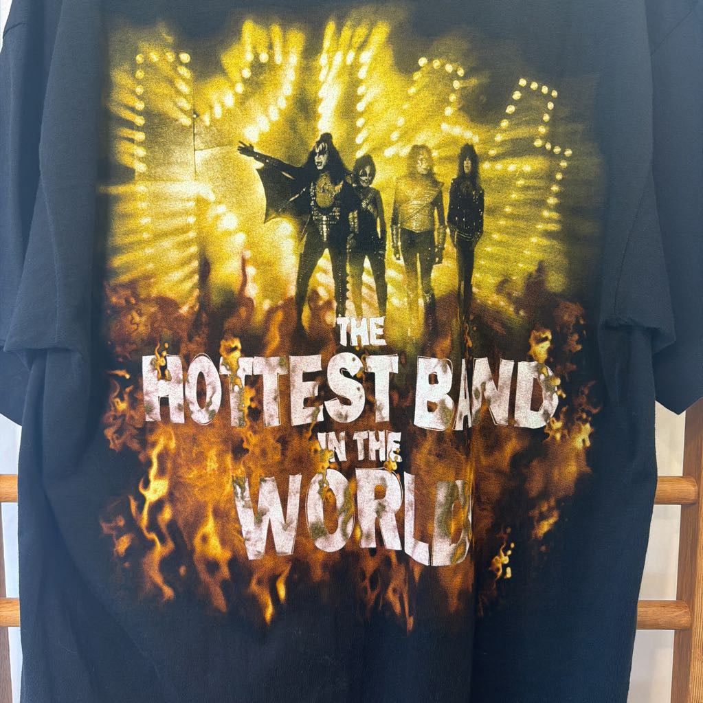A dark navy blue graphic t-shirt featuring a large front print of the band 'The Hottest Band in the World' with stage lights, silhouettes of band members, and flames.