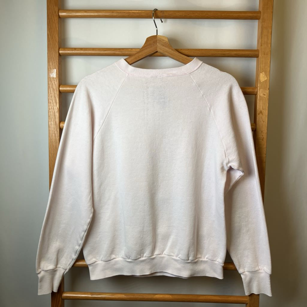 Beige sweatshirt hanging on a wooden rack against a plain wall.