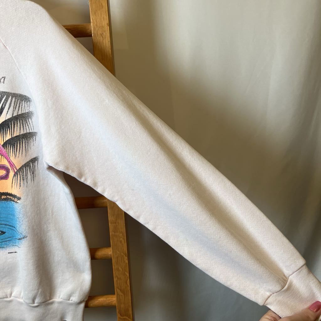Beige sweatshirt with a colorful graphic on a wooden hanger against a neutral wall.