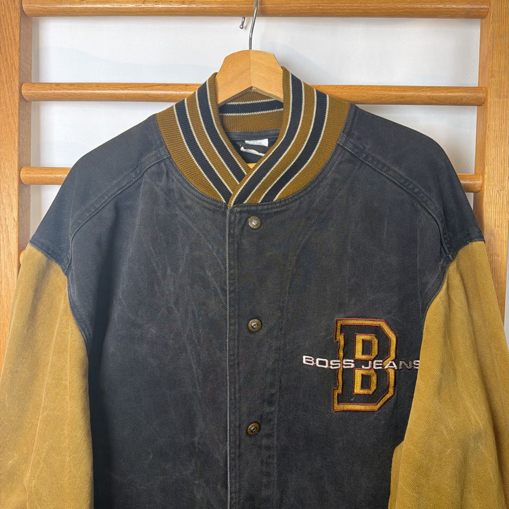 Letterman jacket with yellow sleeves and a visible brand logo on a wooden rack.
