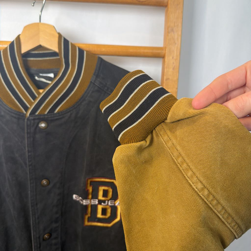 Black and yellow varsity jacket with a visible brand logo on a wooden hanger.
