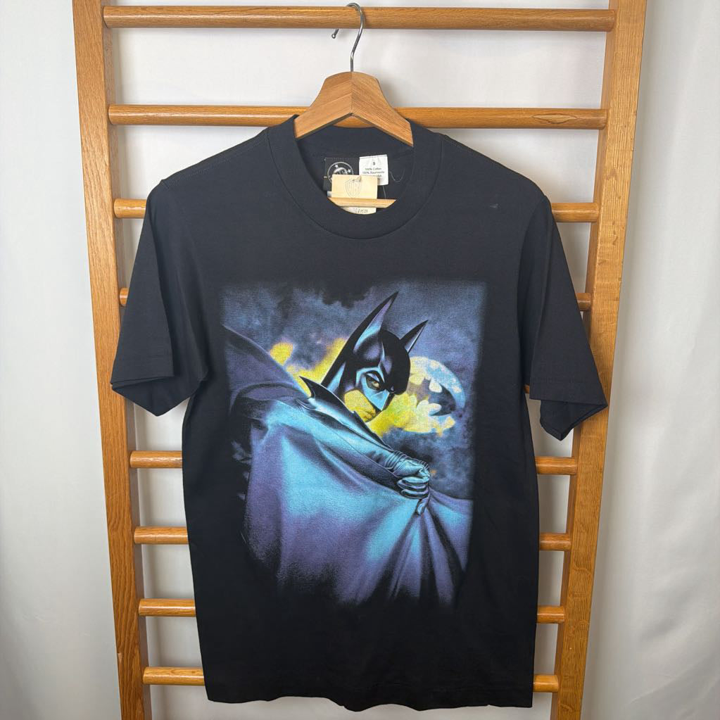 Black t-shirt with Batman graphic on a wooden hanger against a white wall.