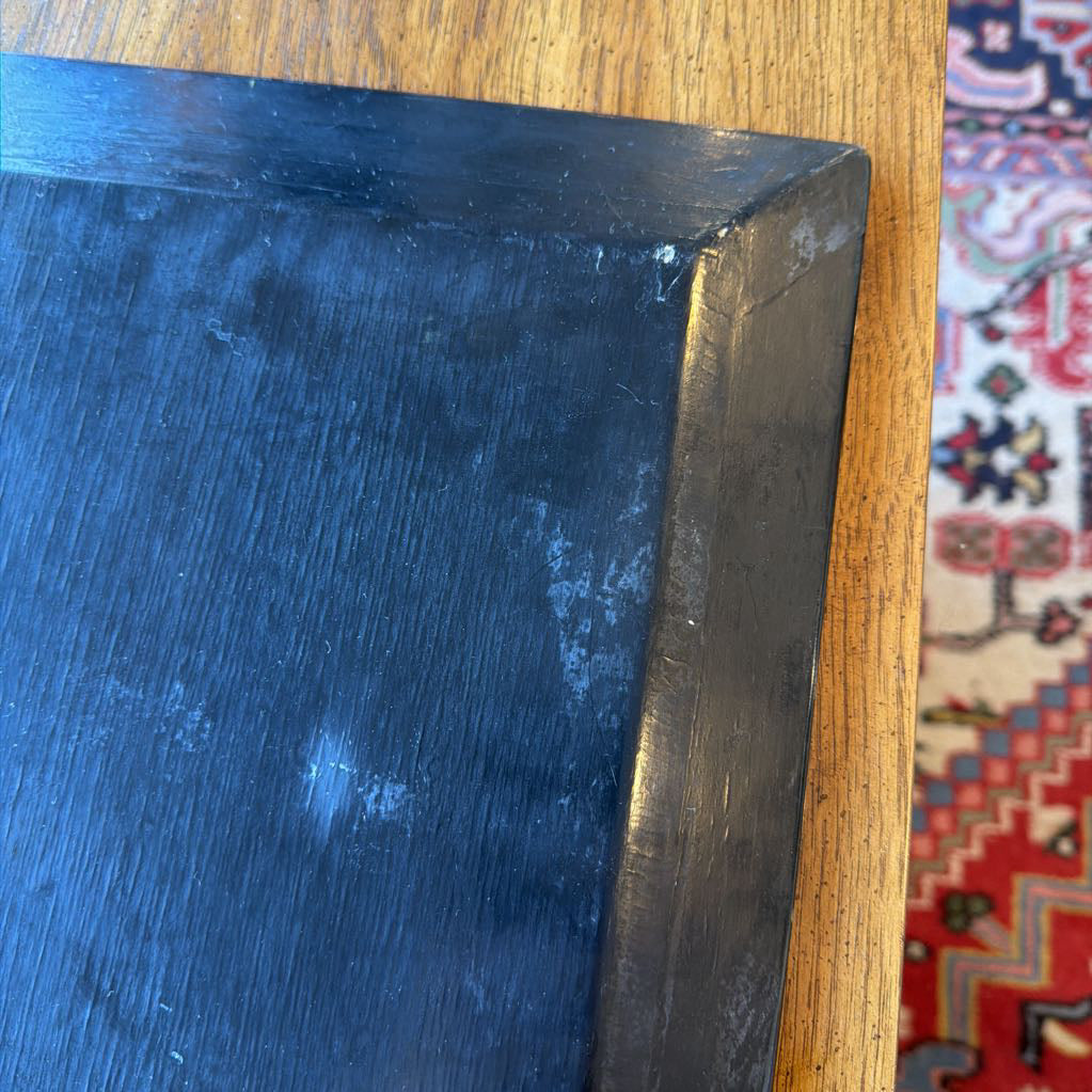 Dark blue rectangular object on a wooden surface with a colorful patterned rug in the background