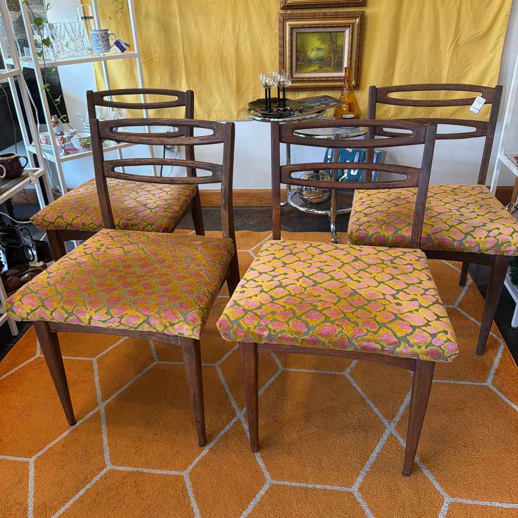 Four wooden chairs with floral cushions on a patterned floor.