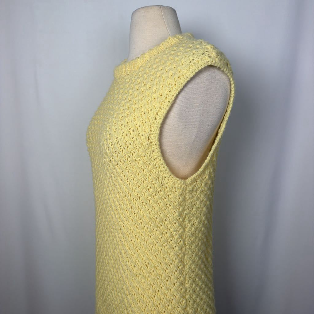 A pale yellow sleeveless knit top displayed on a cream dress form mannequin against a light gray fabric backdrop.