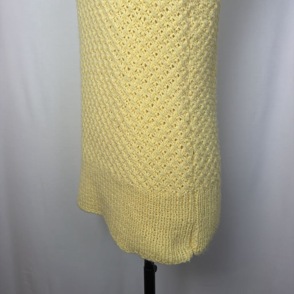 A pale yellow knit sweater or cardigan sleeve with a textured diamond knit pattern and ribbed hem, displayed on a black mannequin stand against a light gray fabric backdrop.