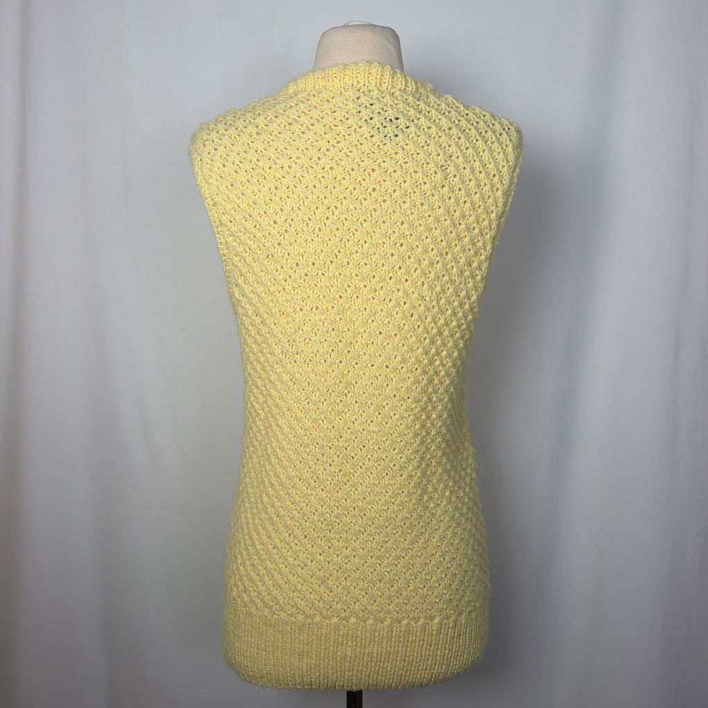 A pale yellow knit sweater vest displayed on a dress form mannequin against a light gray fabric backdrop.