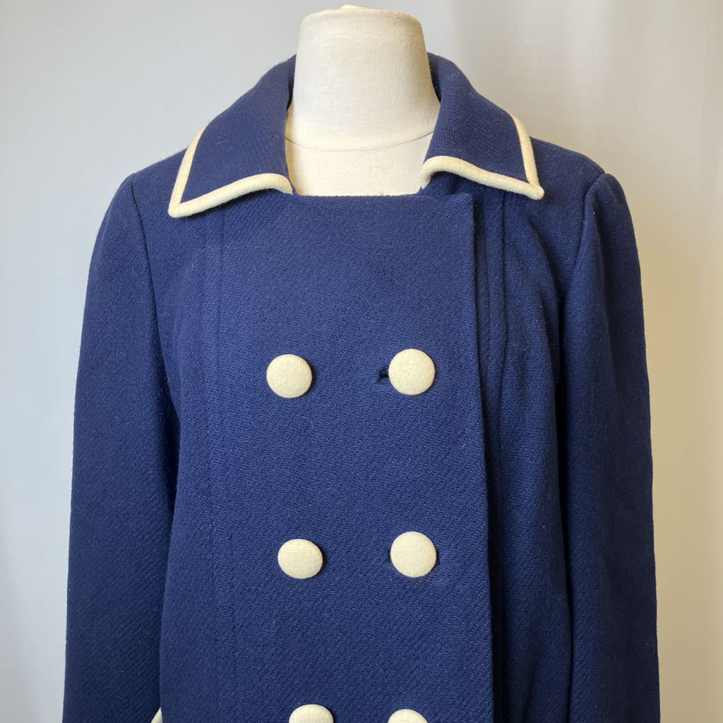 Blue coat with white buttons on a mannequin against a neutral background