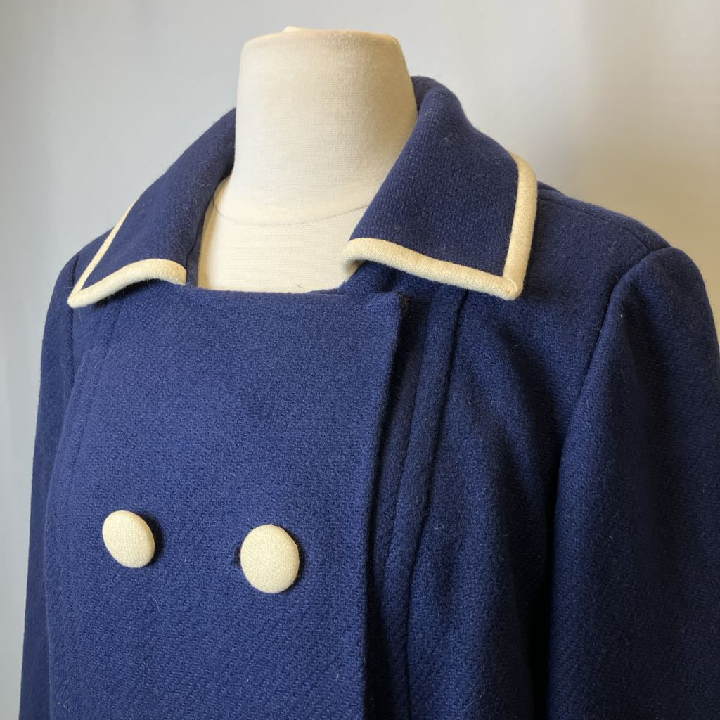 Blue coat with white buttons on a mannequin against a neutral background