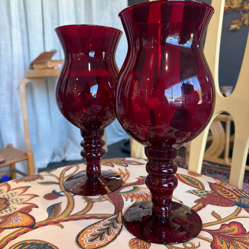 Two red glass goblets on a patterned tablecloth with a blurred indoor background.