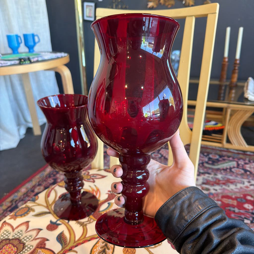 Red goblet held by a hand in a home setting with a chair and table in the background.
