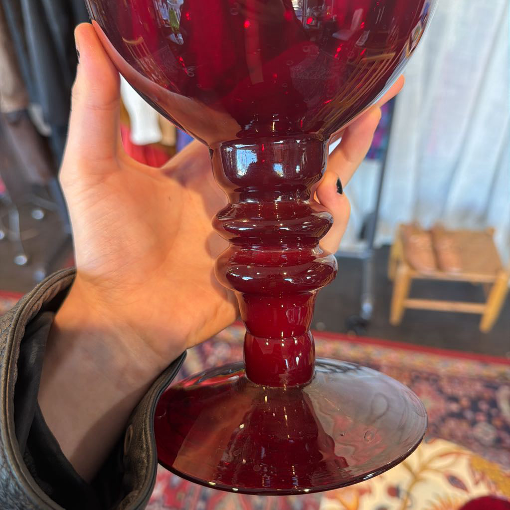 Red glass object held by a hand with a blurred indoor background