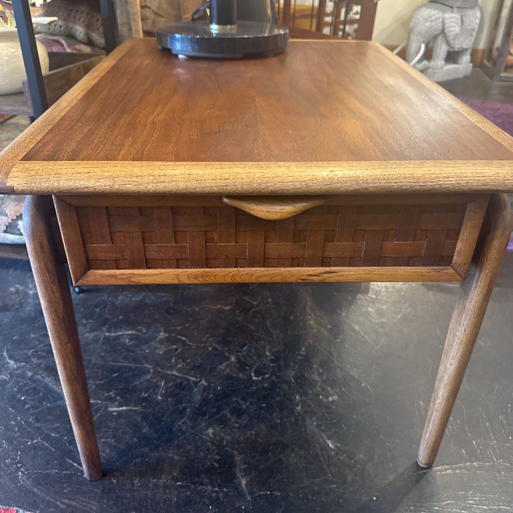 Wooden side table with woven basket drawer on a dark floor.