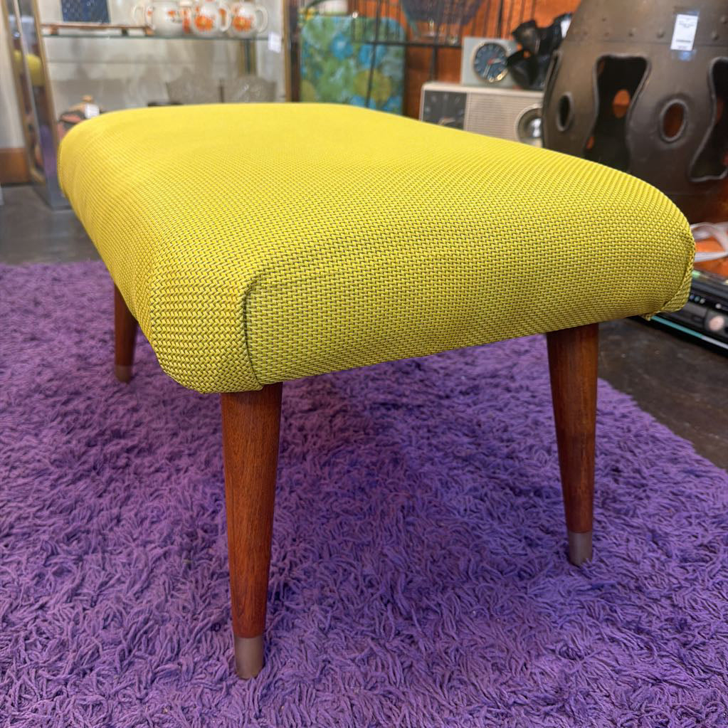 Yellow upholstered stool with wooden legs on a purple rug