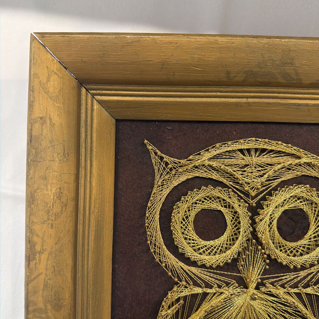 framed bronze owl string art against a dark brown fabric background