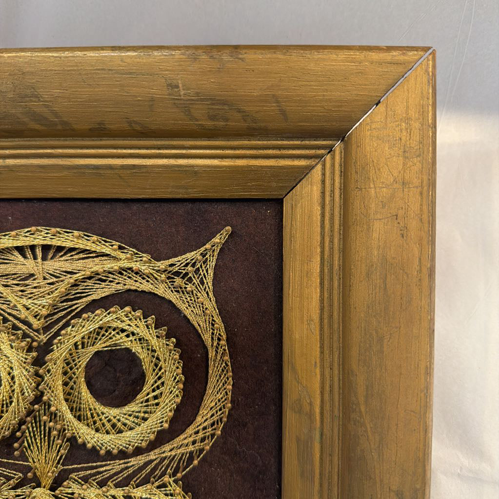 framed bronze owl string art against a dark brown fabric background