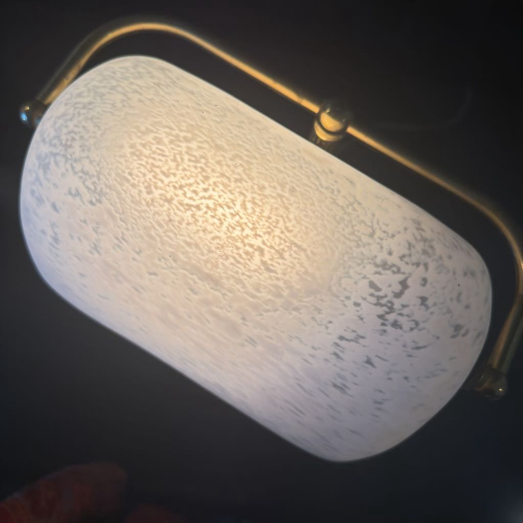 Light fixture with textured white shade and gold arm on a dark background