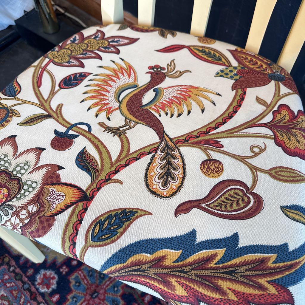 Decorative cushion with intricate floral and bird pattern on a chair.