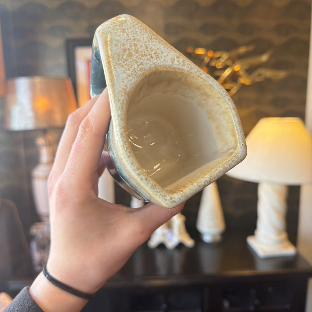 Hand holding a ceramic pot with a textured surface in a room with lamps and decor.