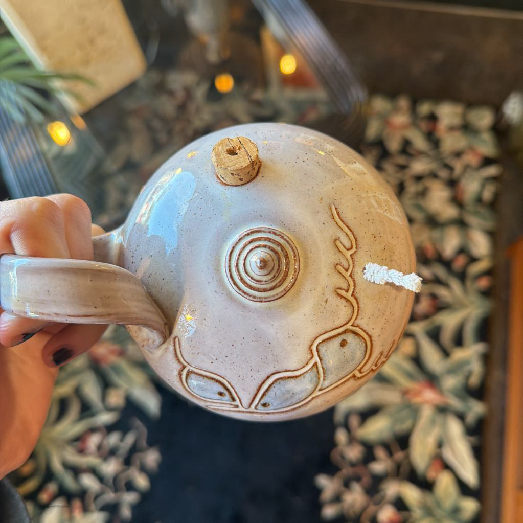 Ceramic teapot with decorative design held by a hand against a blurred background
