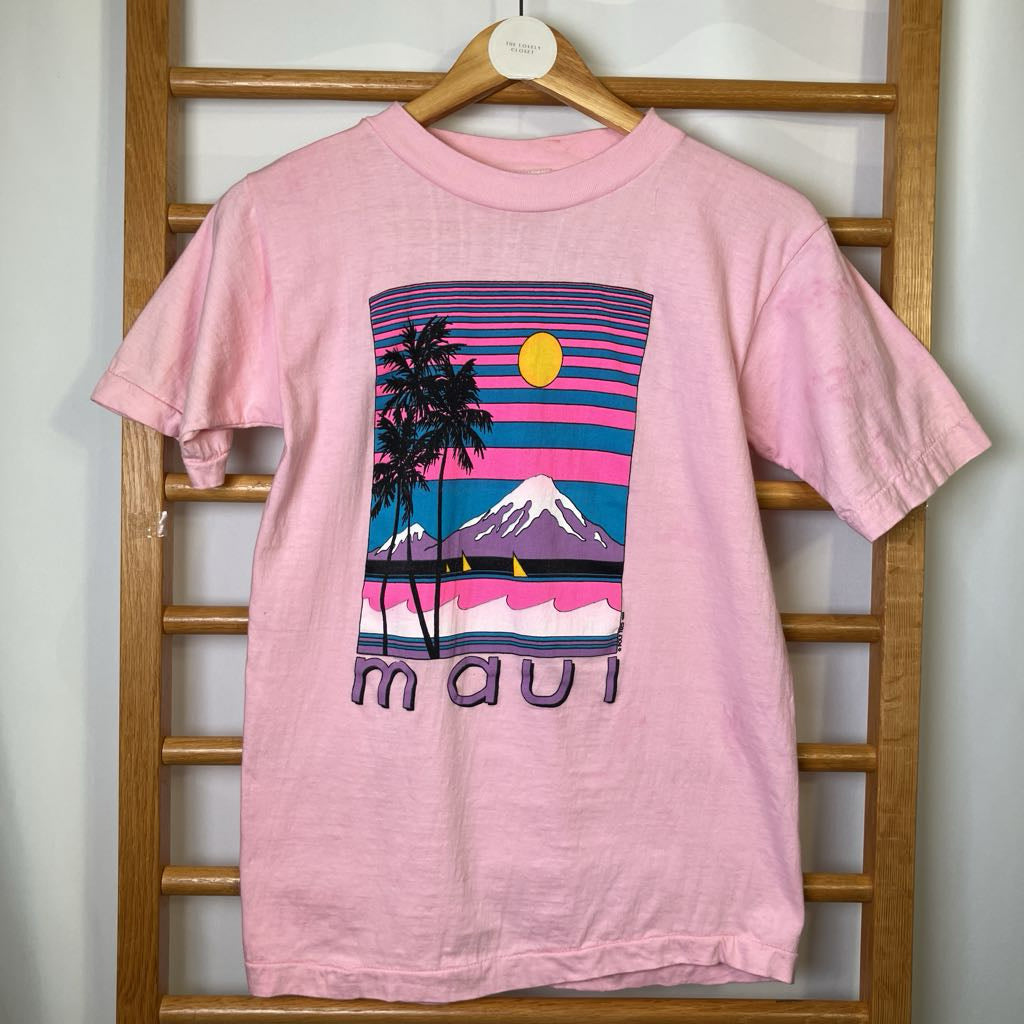 Pink t-shirt with a colorful graphic and 'maui' text on a wooden rack.