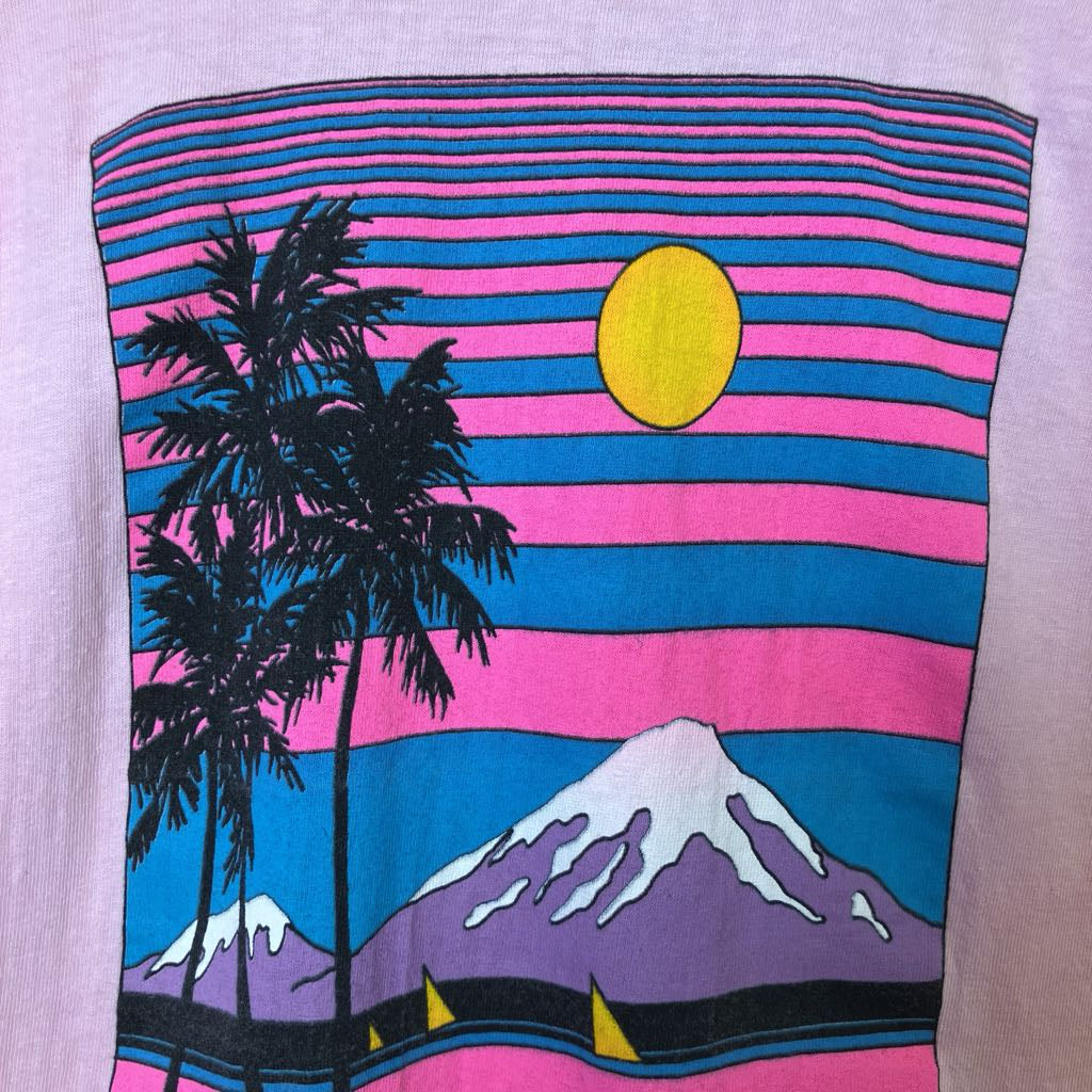T-shirt with a colorful design of palm trees, mountains, and a sun on a striped background.