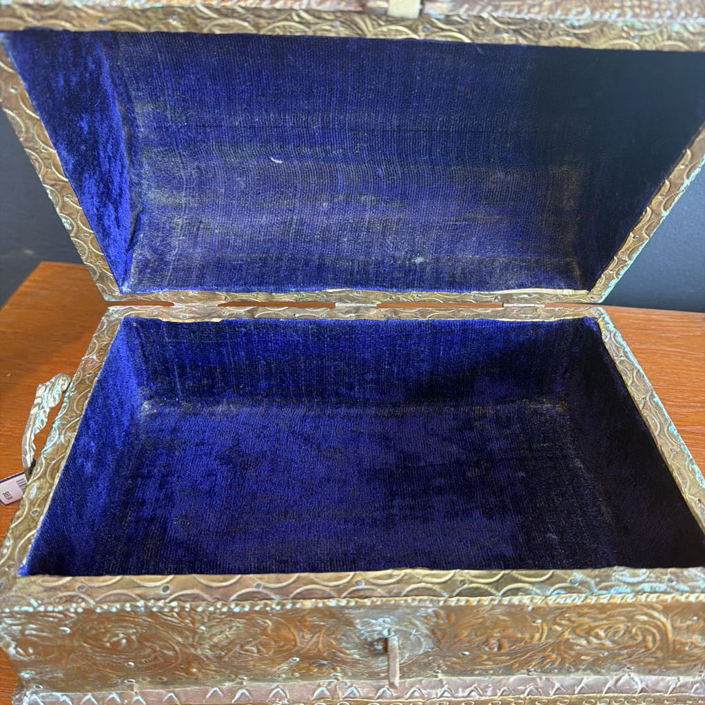 Decorative jewelry box with blue interior and ornate gold exterior on a wooden surface.
