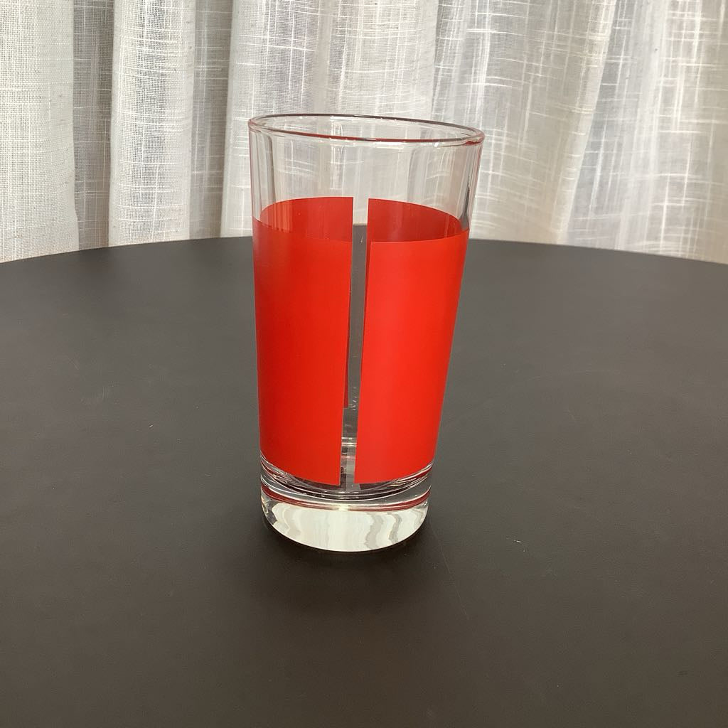 Clear glass with red accent on a dark surface and light curtain background