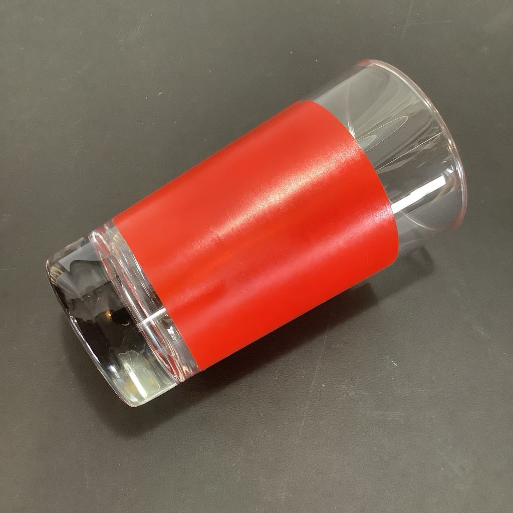 Clear cylindrical glass with a red top on a gray surface