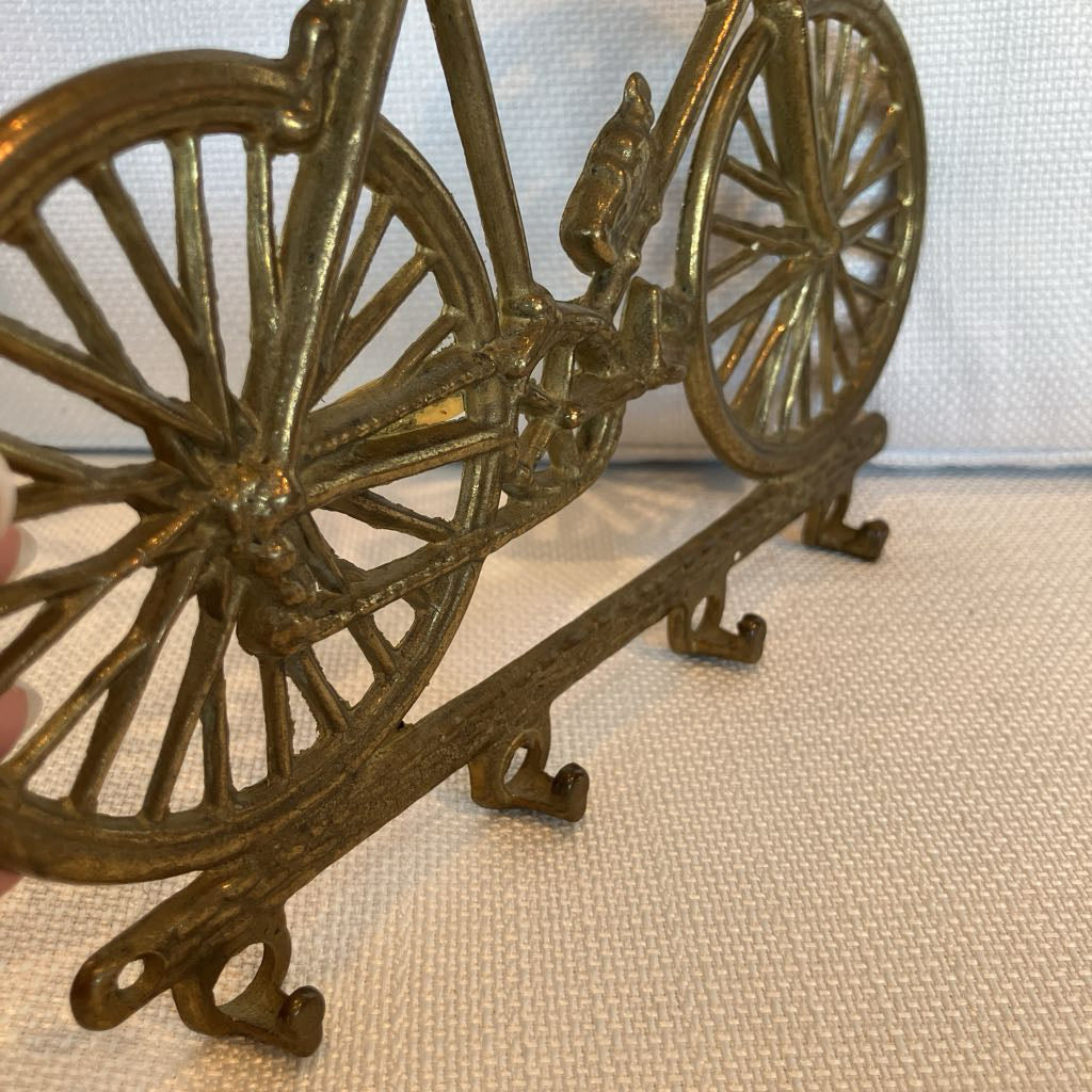 Brass bicycle-shaped wall hook on a textured surface