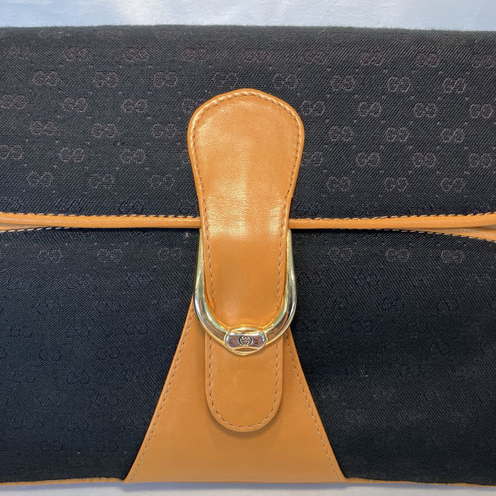 Close-up of a Gucci clutch bag featuring a black GG Supreme canvas body, a tan leather strap, and a gold-tone metal D-ring clasp.