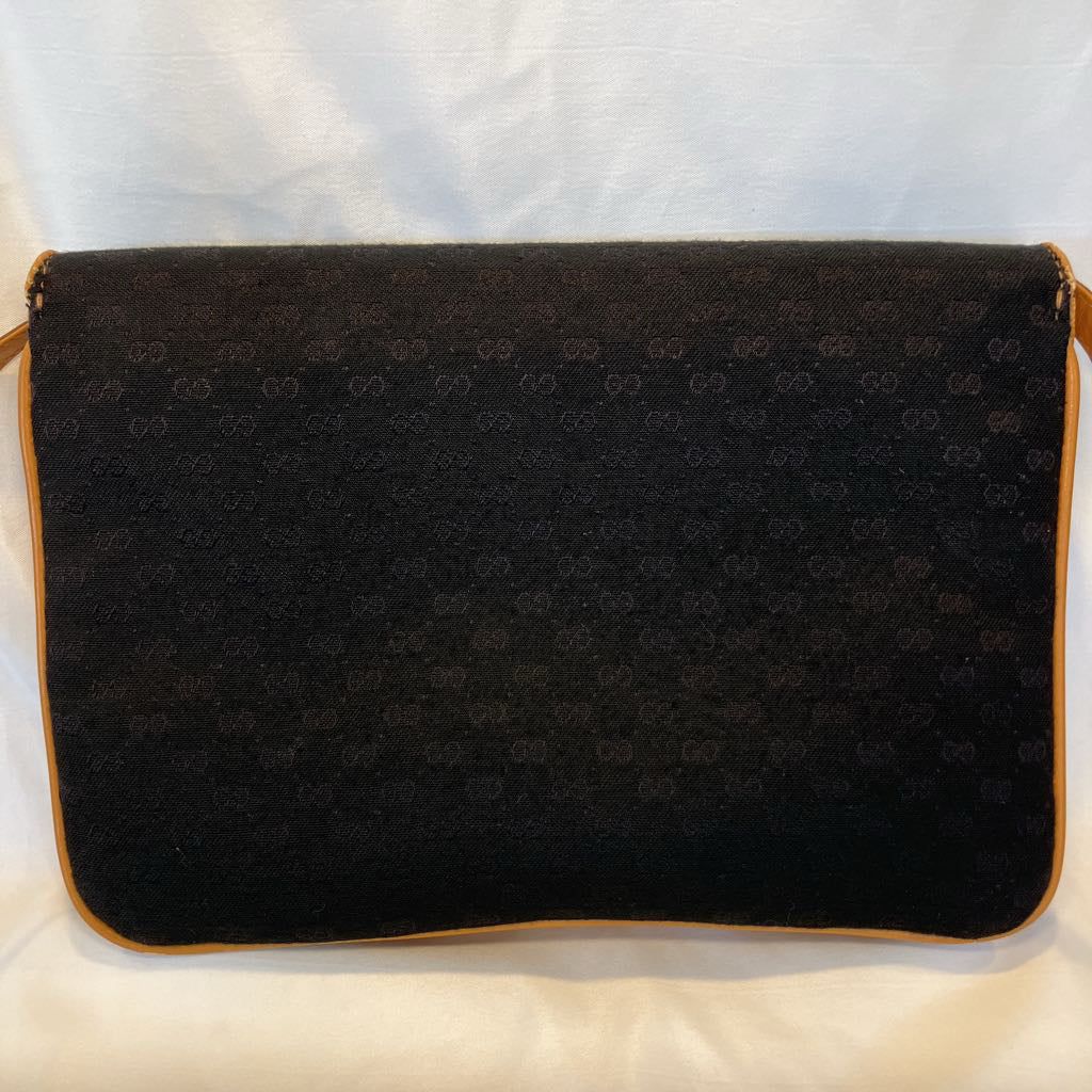 A black Gucci shoulder bag with the brand's signature GG monogram pattern and tan leather trim, photographed against a white fabric background.