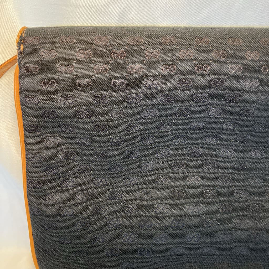 A close-up of a dark gray woven fabric with an allover repeating monogram pattern, showing a thin orange trim along the left edge.