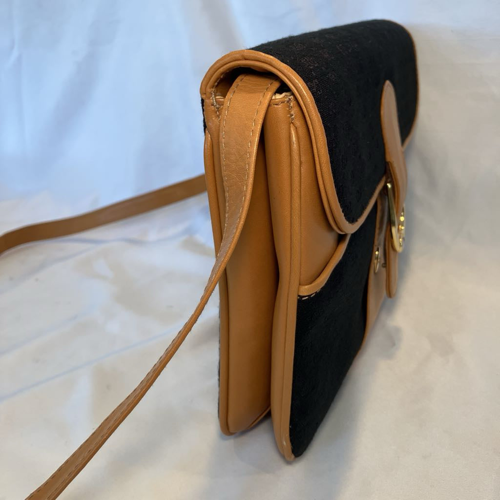 A black and tan crossbody handbag with a long shoulder strap, shown from a side angle on a white fabric background.