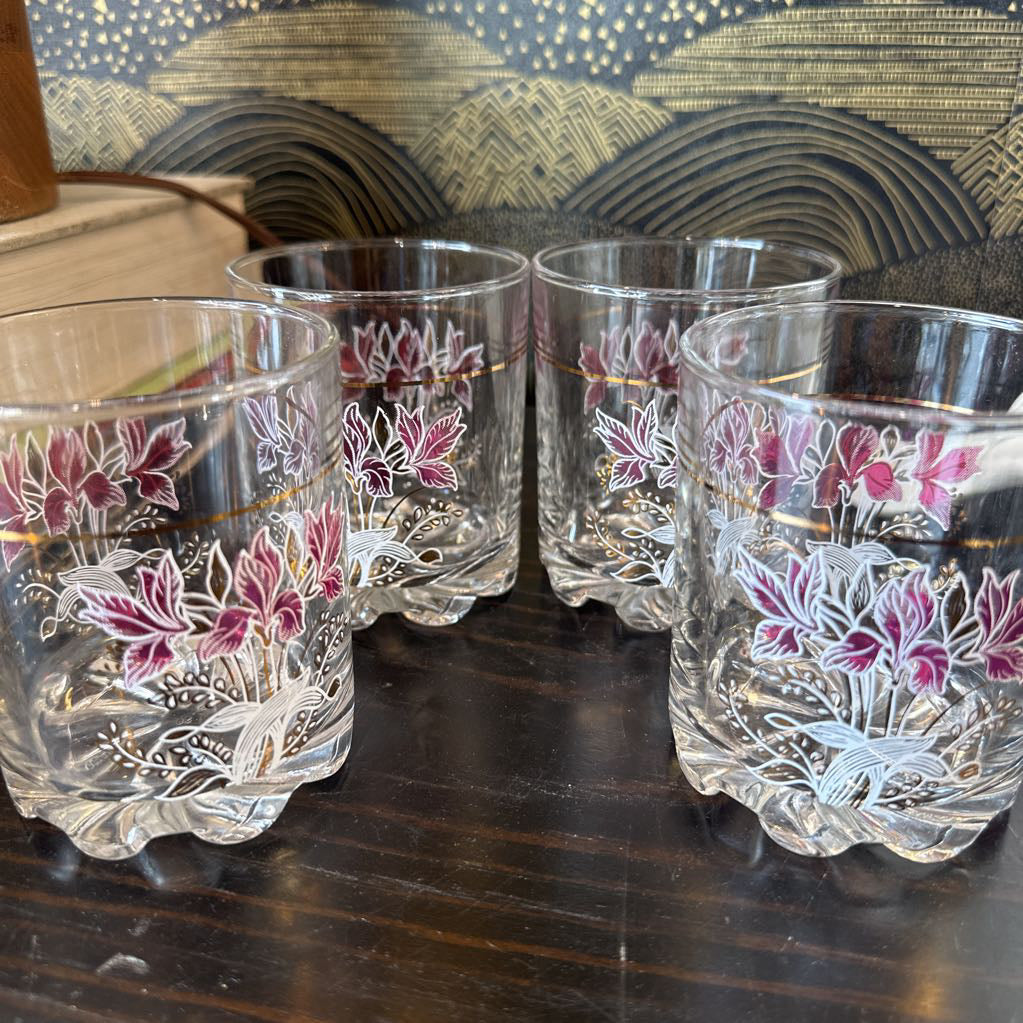 Set of four floral-patterned glasses on a wooden surface with a decorative background.