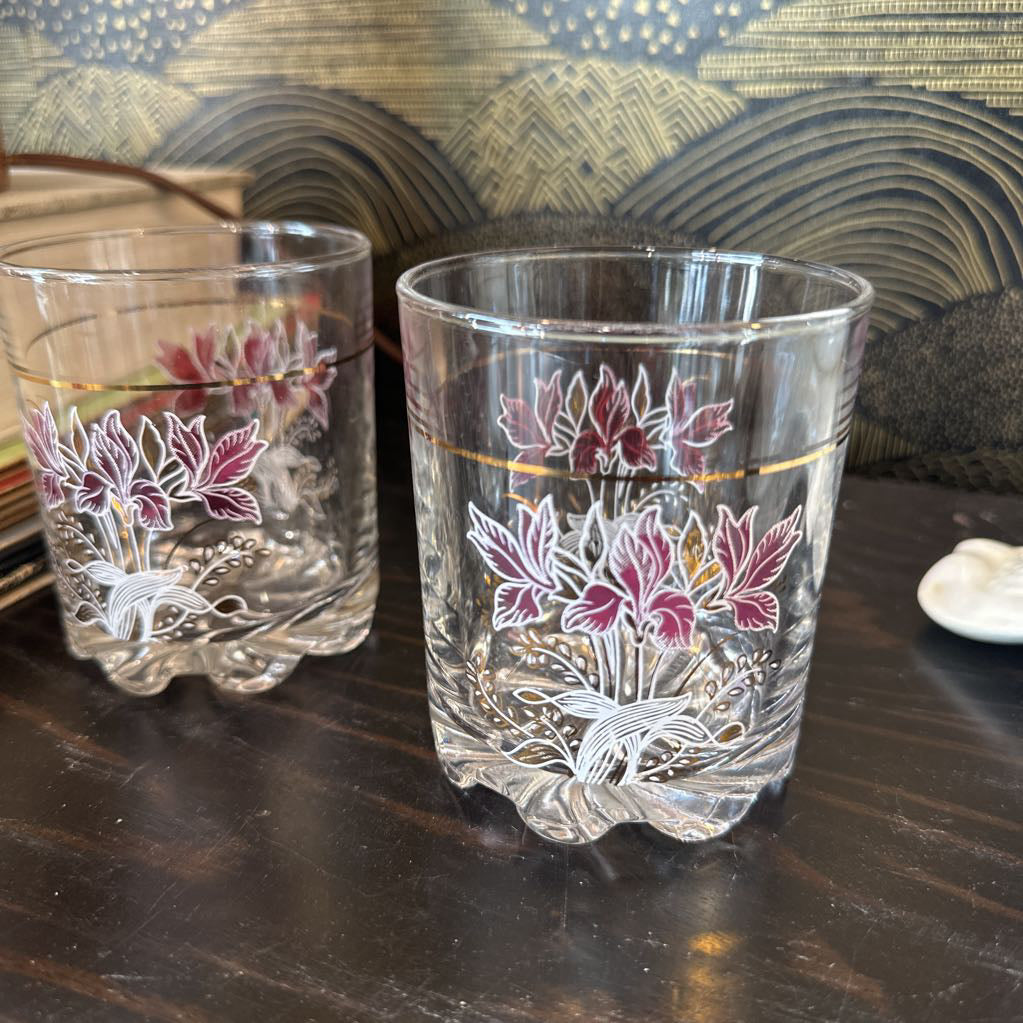 Two floral-patterned glass tumblers on a wooden surface with a decorative background.
