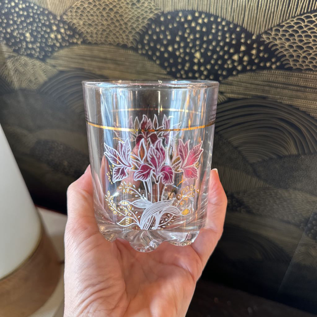 Hand holding a clear glass with floral design against a textured fabric background