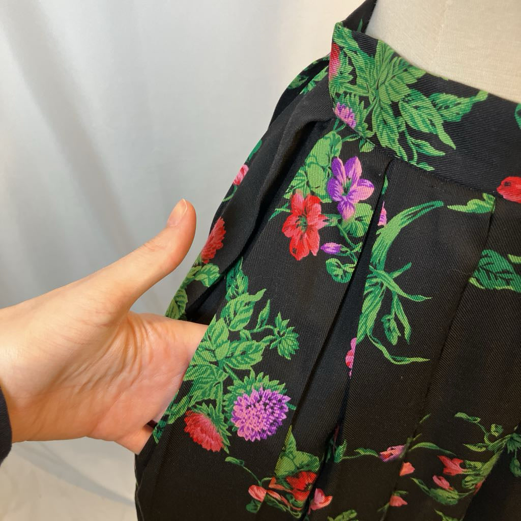 Black fabric with colorful floral pattern held by a hand on a neutral background