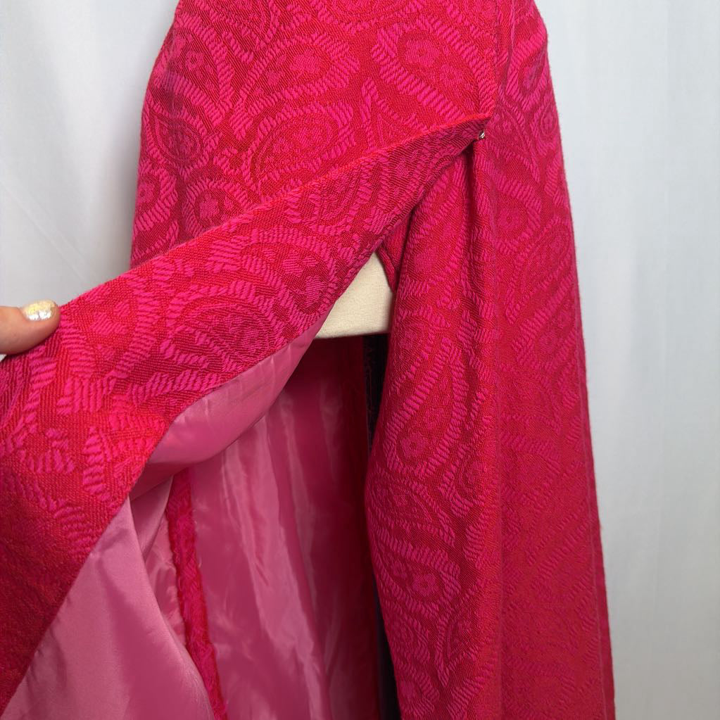 Close-up of a red fabric with a pattern held by a hand against a white background