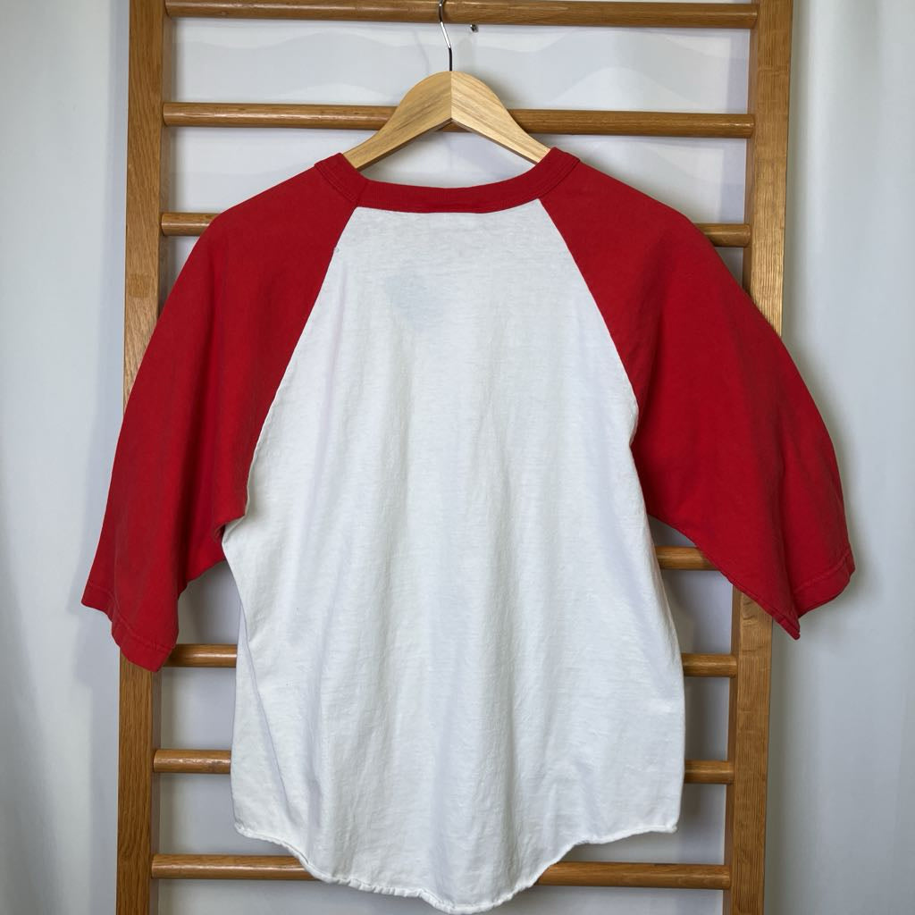 Red and white baseball shirt on a wooden hanger against a white wall.