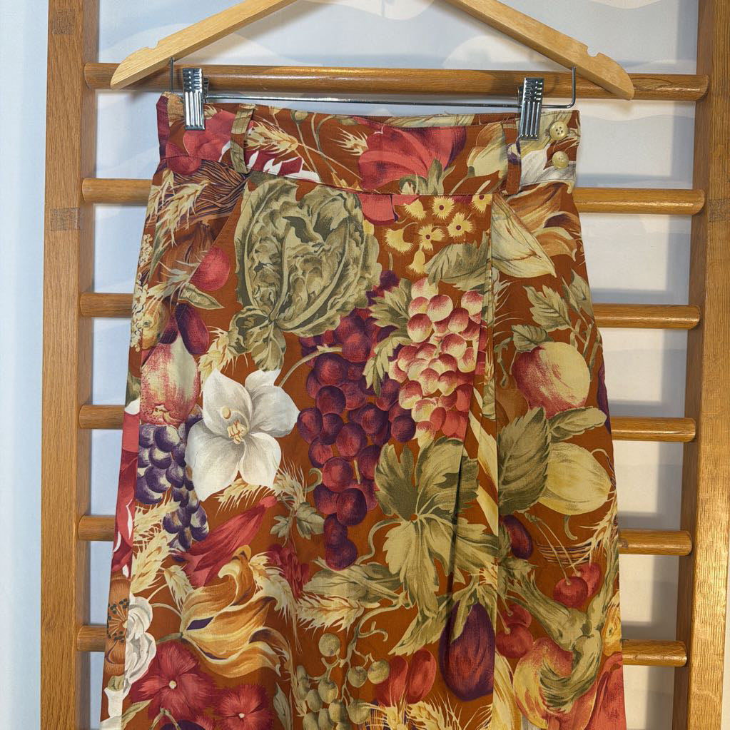 Floral and fruit patterned skirt on a wooden hanger against a white wall.