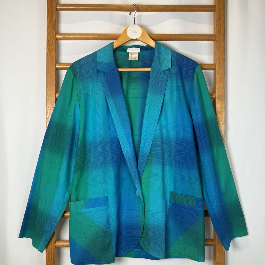Blue and green gradient jacket on a wooden hanger against a white wall.
