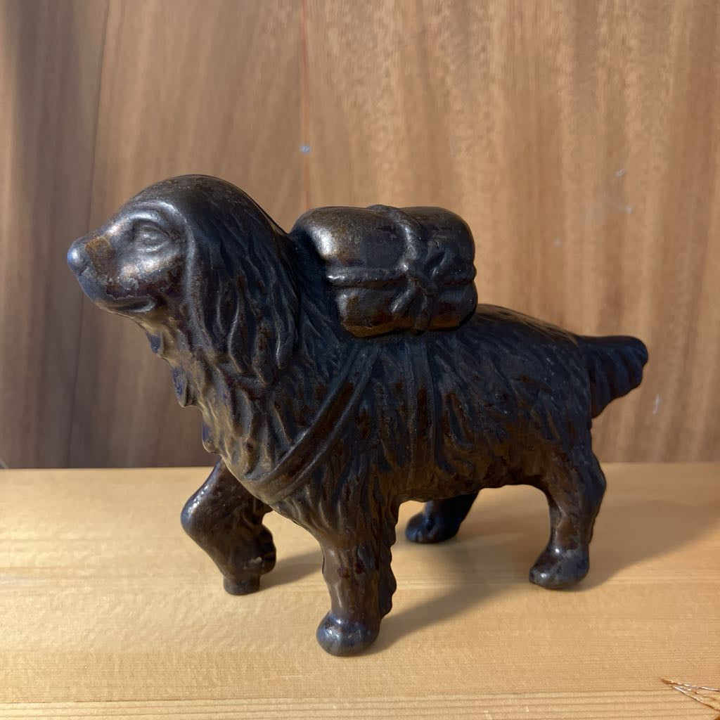 Bronze statue of a dog with a backpack on a wooden surface