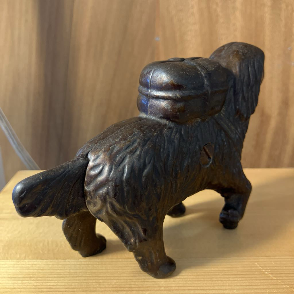 Bronze-colored metal dog figurine on a wooden surface with a neutral background