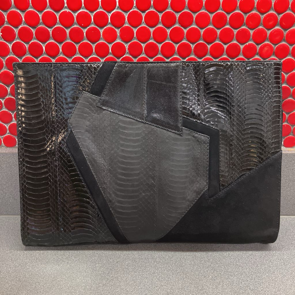 Black textured clutch bag on a gray surface with a red tiled background