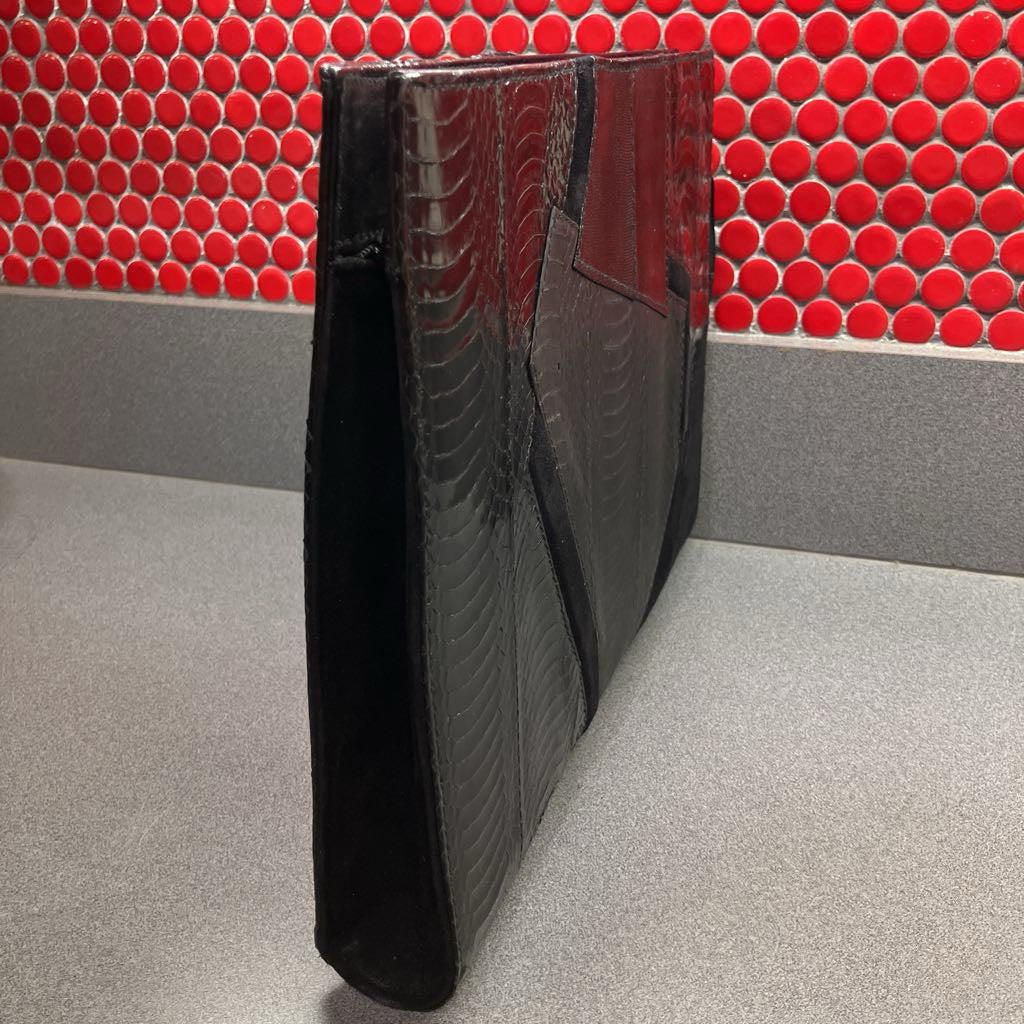 Black textured clutch bag on a gray surface with a red tiled wall background