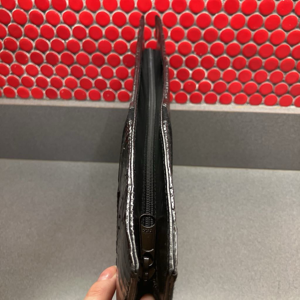 Black clutch bag held in front of a red tiled wall