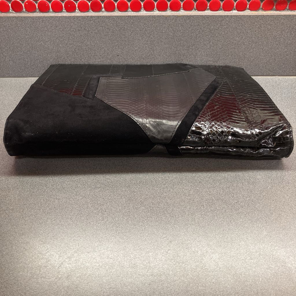 Black textured clutch bag laying on a gray surface with red circular objects in the background