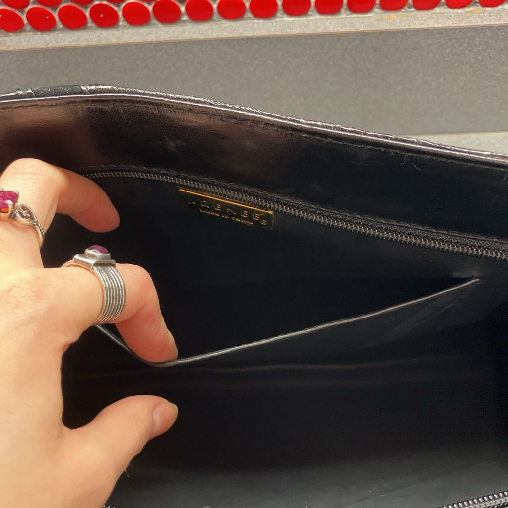 Hand opening a black clutch bag with a visible brand logo.